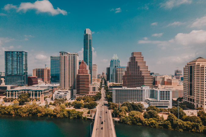 Aerial view of Cypress, Texas skyline featuring modern commercial buildings, a bridge over a waterway, tree-lined streets, and a bright blue sky.
